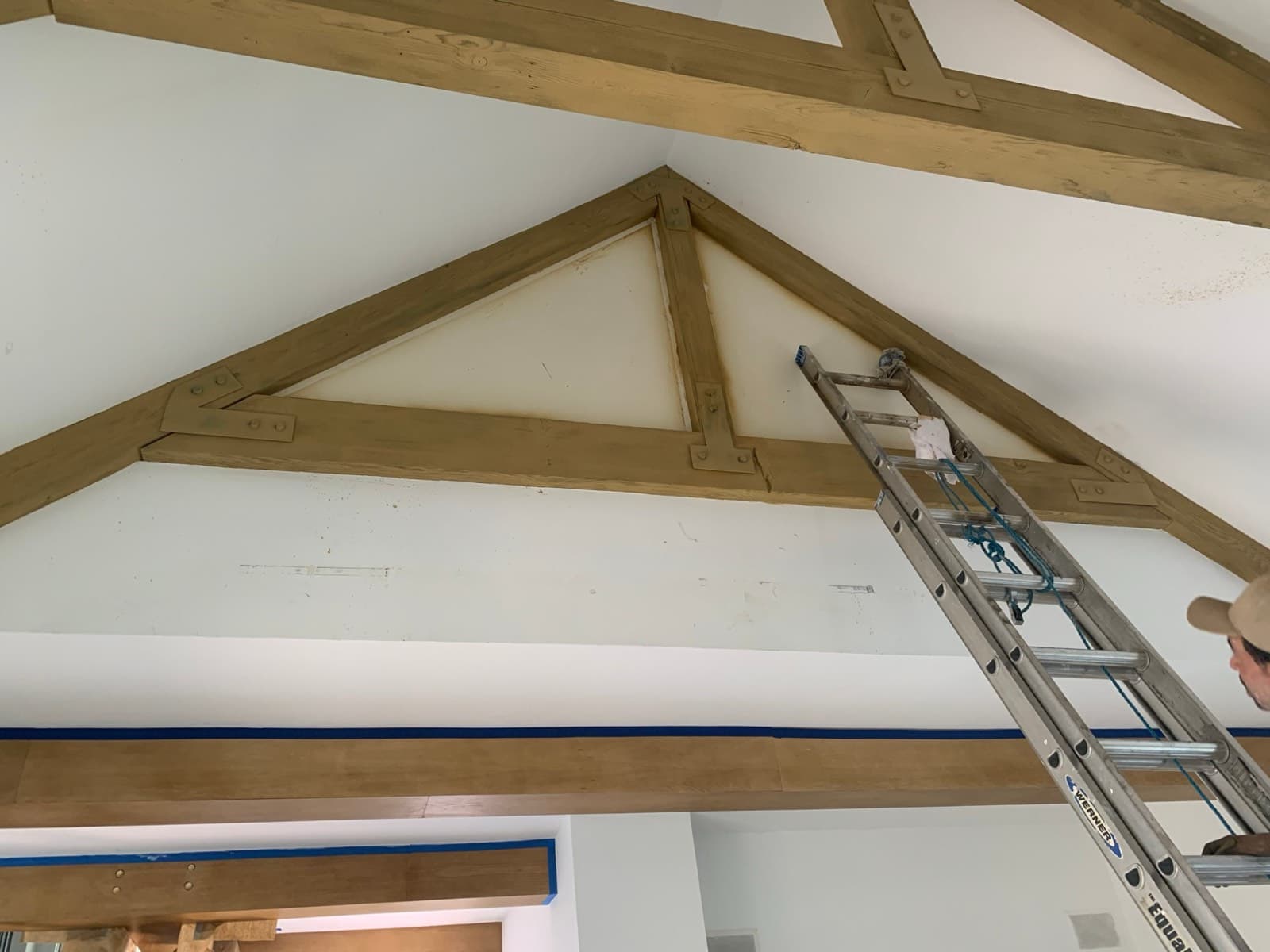 Vaulted ceiling with beams and edges masked in blue tape during preparation