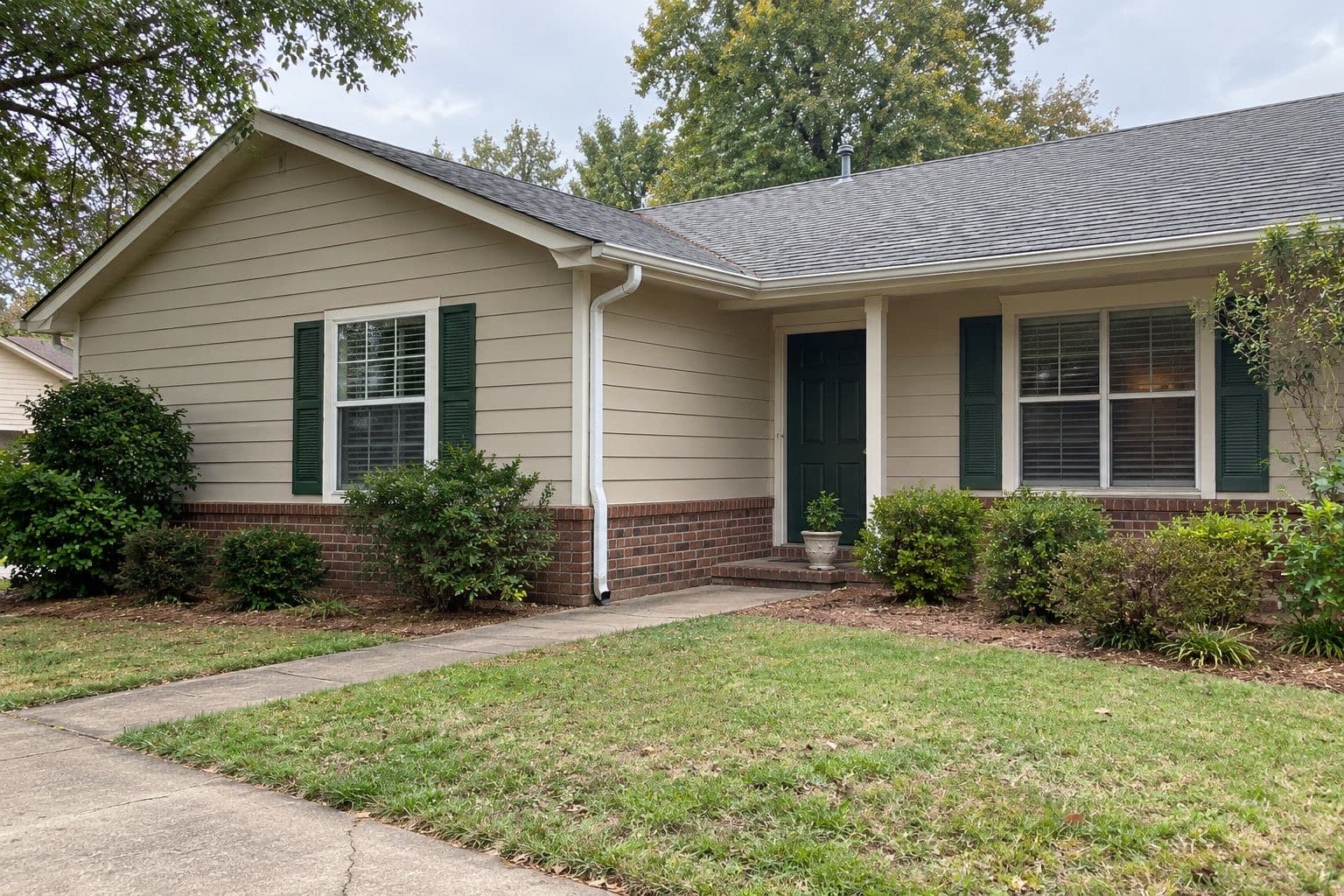 Ranch home with tan lap siding, white trim and dark green shutters and front door
